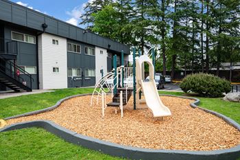 A playground with a slide and swings in front of a building.